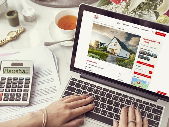Laptop mit Hausbau-Webseite, Taschenrechner und Unterlagen zur Finanzierungsplanung beim Hausbau mit AN Massivhaus