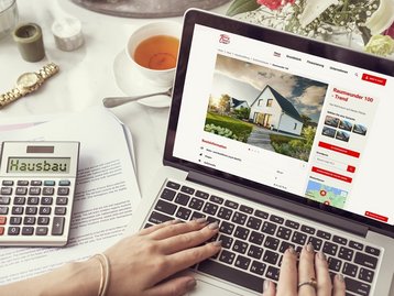 Laptop mit Hausbau-Webseite, Taschenrechner und Unterlagen zur Finanzierungsplanung beim Hausbau mit AN Massivhaus